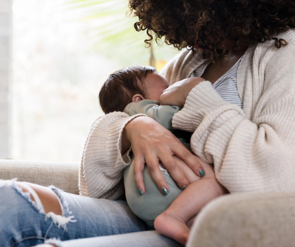 A very close up photo of a woman breastfeeding her baby. The woman's face is obscured by her curly hair as she leans over her baby. Her baby is dressed in a baby grow.