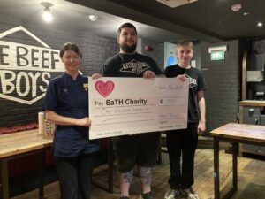 Nurse with Beefy Boys staff holding large charity cheque.